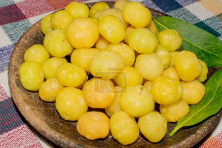 Téléchargez les photos : Canneberge étoilée (Phyllanthus acidus Skeels.) Fruit exotique vert acide, cultivé dans les régions tropicales. servi sur une assiette typique sur une nappe à carreaux - en image libre de droit