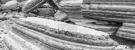 Photo for A captivating black and white panoramic image with large boulders prominently displaying strata. This striking scene captures the dramatic geological formations of the British coastline. - Royalty Free Image