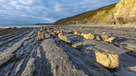 Photo for A breathtaking landscape photograph capturing the rocky seashore bathed in the warm glow of evening sunlight, with boulders dotting the coastline leading to the sea cliffs and Aberystwyth. - Royalty Free Image