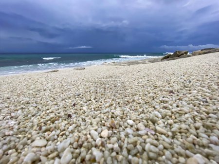 Téléchargez les photos : Scène tranquille de galets brillants sur la plage de Thoondu, Fuvahmulah, Maldives, avec des vagues se brisant et des nuages sombres au-dessus. Vue relaxante sur la côte. - en image libre de droit