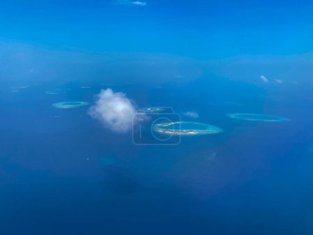 Foto de Espectacular vista aérea de un grupo de islas Maldivas rodeadas de aguas turquesas y una sola nube esponjosa en el cielo azul. - Imagen libre de derechos