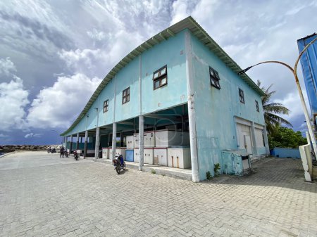 Foto de Edificio tradicional del mercado de pescado de Maldivas con un techo curvo azul claro, situado contra un cielo dramático. Exóticas vibraciones isleñas y vibrantes paisajes costeros. - Imagen libre de derechos