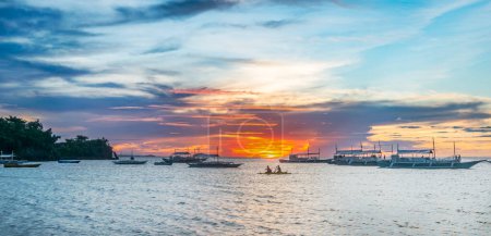 Photo for Silhouette of two adventurers canoeing amidst dive boats at sunset in Malapascua, Philippines. Serene tropical evening by the sea. - Royalty Free Image