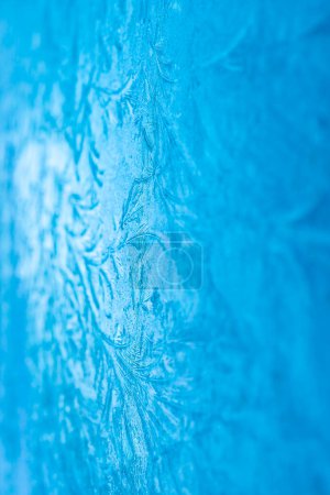 Aufwändige Frostmuster auf Glas schaffen einen atemberaubenden blauen abstrakten Hintergrund, perfekt für winterliche Konzepte.