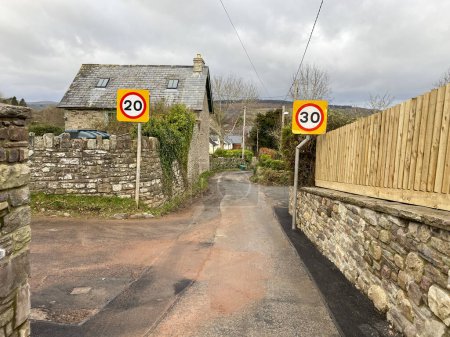 Humorvolle Straßenszene mit kollidierenden 20 km / h und 30 km / h-Tempolimit-Schildern auf der gegenüberliegenden Straßenseite, die Verwirrung stiften. Wales, Großbritannien.