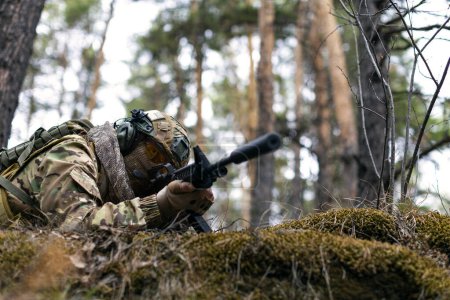 Photo of a soldier aims at the enemy during a clash in the forest. The concept of modern warfare and special forces. Cropped image.