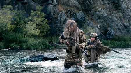 Téléchargez les photos : Photo of two mercenary soldiers crossing the river after the completion of the sabotage operation. Soldiers covertly leave the combat area, fording across the river. - en image libre de droit