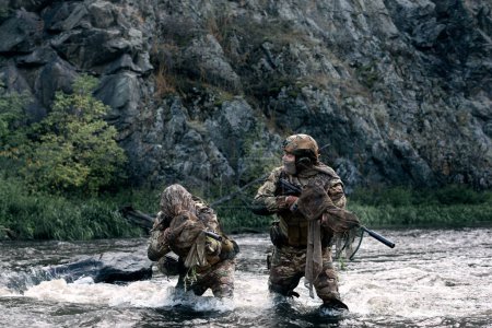 Téléchargez les photos : Photo of two mercenary soldiers fording across the river after the completion of the sabotage operation. Soldiers covertly leave the combat area. - en image libre de droit