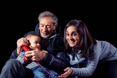 Foto de Retrato de niño sonriente abrazándose con sus padres sentados en el fondo negro - filmado en el estudio - Imagen libre de derechos