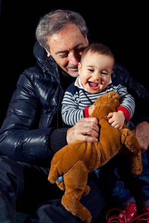 Photo for Portrait of smiling little boy hugging with his parents sitting on black background - studio shot - Royalty Free Image