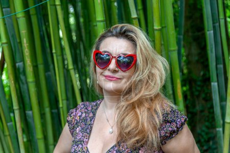 Téléchargez les photos : Portrait d'une belle femme d'âge moyen devant un bosquet de bambou dans un jardin à la française - concept de vacances d'été - en image libre de droit