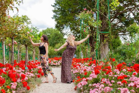 Téléchargez les photos : Deux belles copines d'âge moyen visitant un jardin plein de fleurs en france - concept de vacances - en image libre de droit
