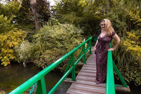 Téléchargez les photos : Portrait de belle femme d'âge moyen posant sur un petit pont au milieu d'un parc vert français concept vacances d'été - en image libre de droit