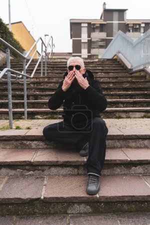 Foto de Hombre maduro rap cantante posando en escaleras al aire libre en las afueras de una gran ciudad - Imagen libre de derechos