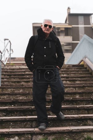 Téléchargez les photos : Homme mature chanteur de rap posant sur les escaliers à l'extérieur à la périphérie d'une grande ville - en image libre de droit