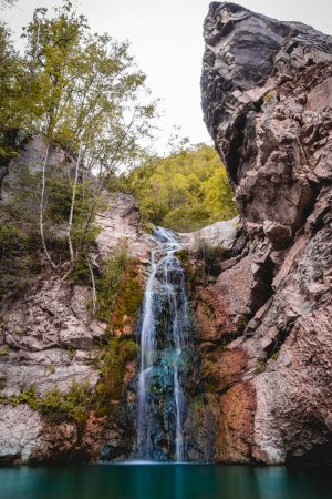 Téléchargez les photos : Magnifique petite cascade qui forme un étang d'eau émeraude dans une forêt d'automne - en image libre de droit