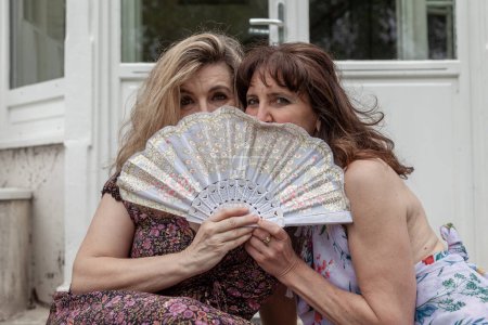 Foto de Pair of beautiful middle aged women waving a vintage fan in front of a french villa - Imagen libre de derechos