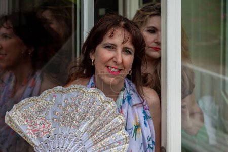 Téléchargez les photos : Pair of beautiful middle aged women waving a vintage fan in front of a french villa - en image libre de droit