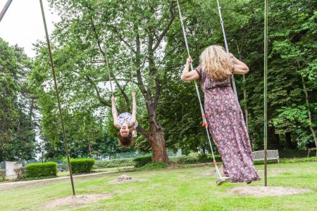 Foto de Beautiful middle aged couple of female friends swinging on children's swings in a french park - Imagen libre de derechos