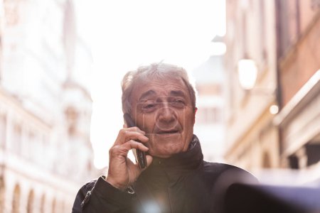 Foto de Portrait of happy retired attractive mature man talking with smart phone on the street in winter - Imagen libre de derechos