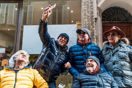 Téléchargez les photos : Group of happy retired mature men taking a selfie with smart phone on the street in winter - en image libre de droit
