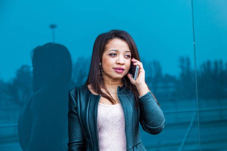 Foto de Pretty business woman talking on mobile smartphone outside in front of a blue mirror - Imagen libre de derechos