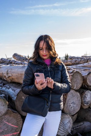 Téléchargez les photos : Femme d'âge moyen portant des vêtements d'hiver en utilisant un téléphone intelligent dans la neige sur une montagne concept de personnes en vacances - en image libre de droit
