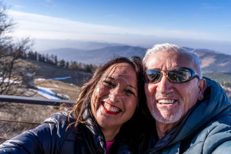 Foto de Pareja de mediana edad con ropa de invierno tomando una selfie sobre una montaña - concepto de personas felices en vacaciones - Imagen libre de derechos