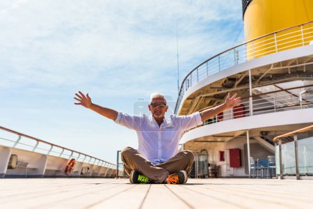 Foto de Feliz apuesto hombre de mediana edad posando sentado en la cubierta de un crucero - viaje y concepto de vacaciones - Imagen libre de derechos
