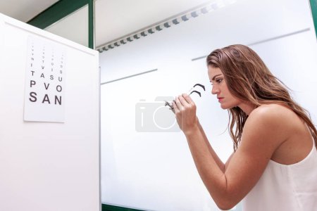 Téléchargez les photos : Belle femme testant de nouvelles lentilles auxiliaires avec phoropter lors d'un examen de la vue dans un cabinet médical - en image libre de droit