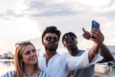 Photo for Small group of multiethnic friends having fun taking a selfie with smartphone - summer vacation concept on a boat sailing on a river - Royalty Free Image