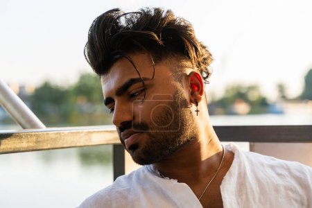 Téléchargez les photos : Portrait de jeune homme indien beau assis sur un bateau naviguant pendant les vacances d'été sur une rivière - en image libre de droit