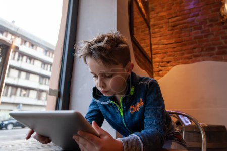 Foto de Niño usando una tableta sentada en un pub frente a una gran ventana - concepto de generación adicta - Imagen libre de derechos
