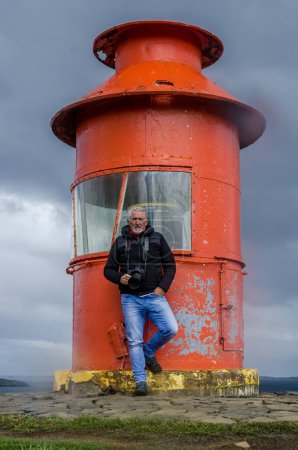 Photo for Middle aged man photographer posing with camera in front of a red lighthouse - vacation concept - Royalty Free Image