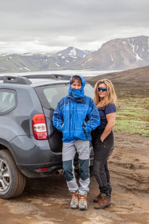 Foto de Dos viajeros de mediana edad posando cerca de un coche en un área salvaje de Islandia - concepto de viaje salvaje - Imagen libre de derechos