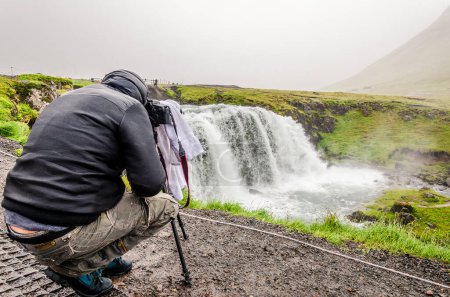 Photo for Middle aged man photographer taking a shot with camera and tripod in front of a majestic waterfall - wilderness vacation concept - Royalty Free Image