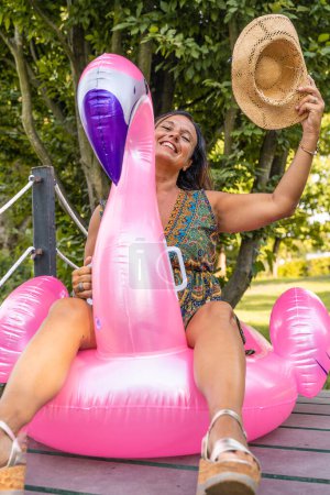 Téléchargez les photos : Portrait de belle femme d'âge moyen assise sur un jouet gonflable rose flamant rose - en image libre de droit