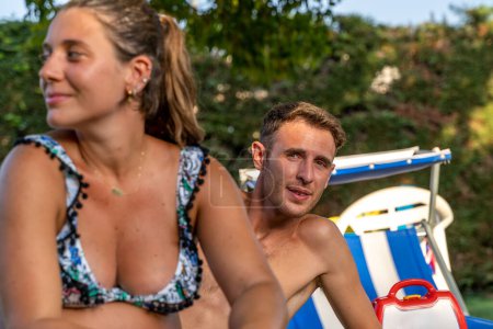 Téléchargez les photos : Drôle de portrait de jeune femme enceinte avec mari en maillot de bain assis sur des chaises de plage dans un resort - en image libre de droit