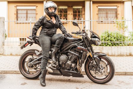 Téléchargez les photos : Femme d'âge moyen en vêtements de motocycliste chevauchant une moto moderne à l'extérieur - en image libre de droit