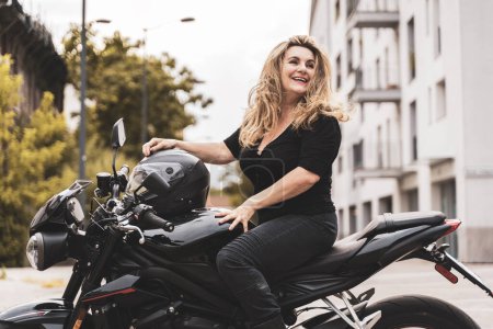 Foto de Mujer de mediana edad en ropa de motociclista montando una motocicleta moderna al aire libre - Imagen libre de derechos
