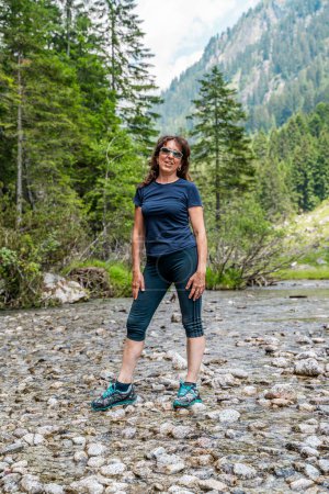 Téléchargez les photos : Belle femme d'âge moyen s'amuser à poser lors d'une promenade dans les montagnes au milieu des pins - en image libre de droit