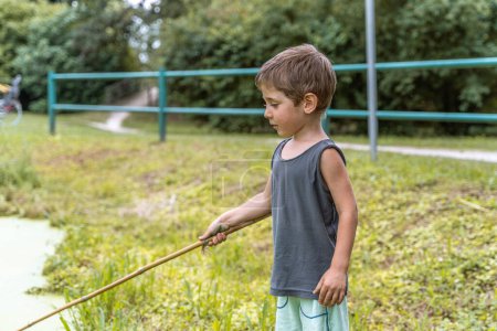 Foto de Pequeño niño sonriente jugando con un palo junto a un estanque en un parque público al aire libre - Imagen libre de derechos