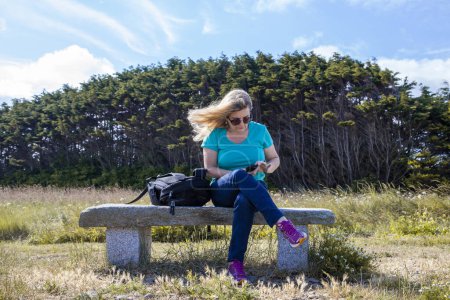 Téléchargez les photos : Belle femme d'âge moyen utilisant le téléphone à l'extérieur dans un environnement naturel assis sur un banc de marbre - en image libre de droit