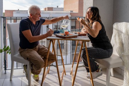 Photo for Beautiful middle aged couple eating Chinese take away food sitting at a laid table in a city balcony - Royalty Free Image