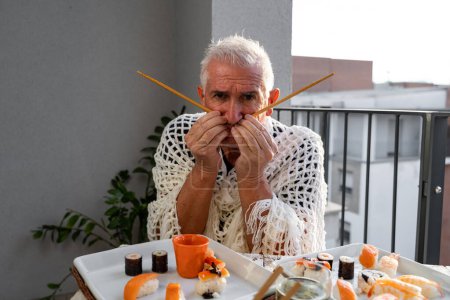 Téléchargez les photos : Attrayant homme d'âge moyen s'amuser assis à une table posée avec de la nourriture à emporter chinois dans un balcon de la ville - en image libre de droit