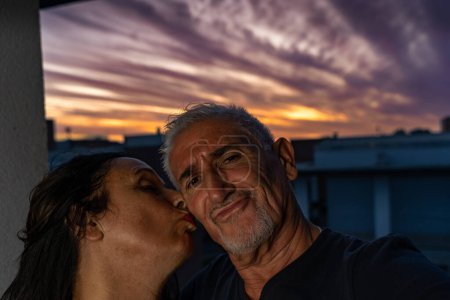 Téléchargez les photos : Beau couple romantique d'âge moyen prenant un selfie sur la terrasse extérieure au coucher du soleil - en image libre de droit