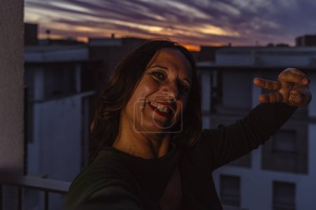 Photo for Beautiful romantic middle aged woman taking a selfie on the outdoor terrace at sunset - Royalty Free Image