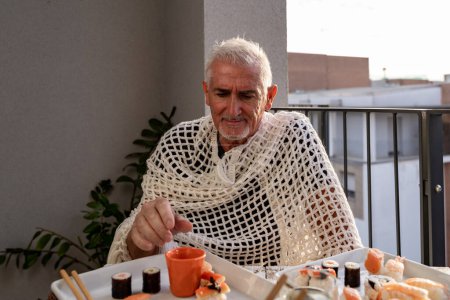 Foto de Atractivo hombre de mediana edad divertirse mientras come sentado en una mesa puso comida china llevar en una terraza al aire libre - Imagen libre de derechos