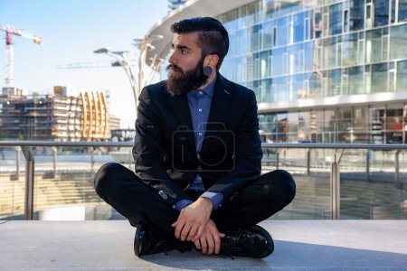 Téléchargez les photos : Jeune hipster élégant relaxant assis à l'extérieur voyageant à travers une capitale européenne - en image libre de droit