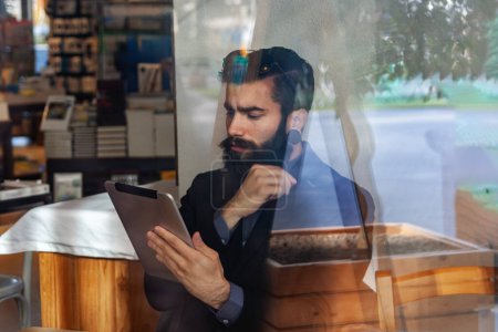 Téléchargez les photos : Jeune homme d'affaires faisant une pause dans un café - vue à travers le magasin jeune homme d'affaires faisant une pause dans un café - vue à travers la vitrine - en image libre de droit